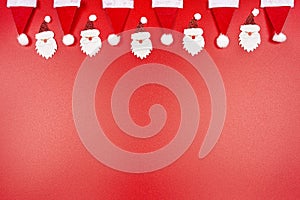 Santa Claus hats and Santa Claus faces made of material arranged in a row on top, isolated on a red background.