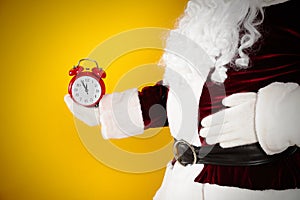 Santa Claus holding alarm clock on yellow background, closeup. Christmas countdown