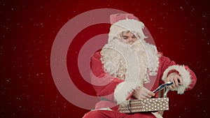 Santa Claus holding Christmas gifts on red background with snow