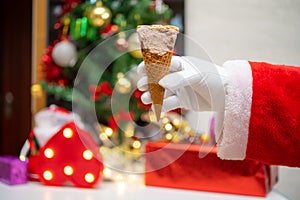 A Santa Claus holding an ice cream cone with couple of bites in front of Christmas decorations at home