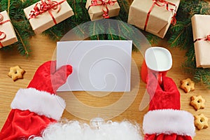 Santa Claus holding letter on wooden table with gift boxes and Christmas tree and cup of hot coffee or tea. mockup blank