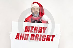 Santa Claus is holding a sign with the inscription - MERRY AND BRIGHT