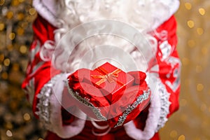 Santa claus is holding small christmas gift red box in both hands. Horizontal