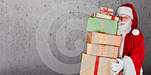 Santa Claus holding a stack of Christmas presents against a plain background with copy space