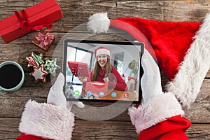 Santa claus holding tablet, making christmas video call with smiling caucasian woman opening gift