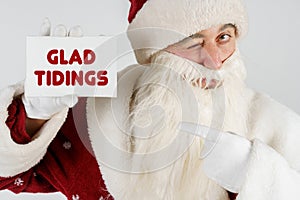 Santa Claus holds a card with the text in his hands - GLAD TIDINGS