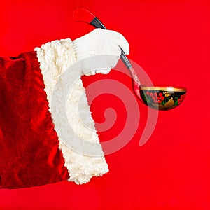 Santa Claus holds in his hand a wooden decorative spoon on a red background, with space for copy.Concept festive cooking,