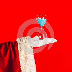 Santa Claus holds a hourglass in his hand on a red background.