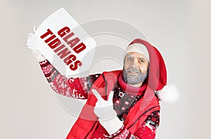 Santa Claus holds a sign with the inscription in his hands - GLAD TIDINGS and points to it with his other hand