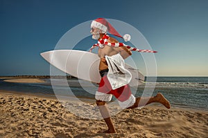 Santa Claus holds towel and surfboard on the beach ÃÂ¾n holiday. Christmas party. Christmas concept