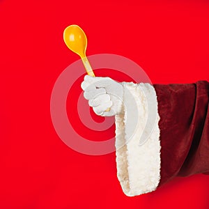 Santa Claus on holiday cooking. Santa Claus hand holding a plastic spoon on a red background. Kitchen and cooking concept