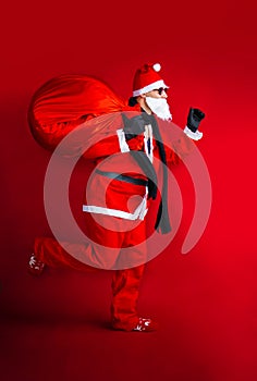 Santa Claus with huge bag, on the run, delivering christmas gifts isolated on red background.