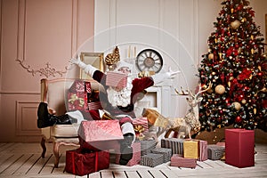 Santa Claus lay down to rest on the sofa with a bunch of gifts near the fireplace and christmas tree . New year and Merry