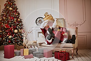 Santa Claus lay down to rest on the sofa with a bunch of gifts near the fireplace and christmas tree . New year and Merry