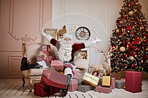 Santa Claus lay down to rest on the sofa with a bunch of gifts near the fireplace and christmas tree . New year and Merry