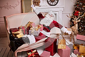 Santa Claus lay down to rest on the sofa with a bunch of gifts near the fireplace and christmas tree . New year and Merry