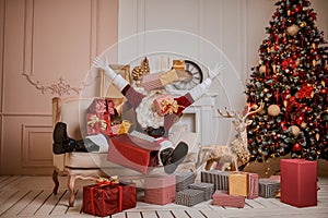 Santa Claus lay down to rest on the sofa with a bunch of gifts near the fireplace and christmas tree . New year and Merry