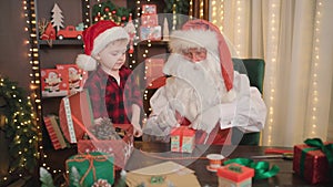 Santa Claus and little assistant boy makes Christmas gifts for children. CHRISTMAS NEW YEAR CONCEPT