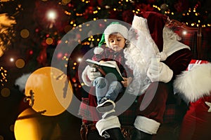 Santa Claus and little boy with book near Christmas tree