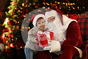 Santa Claus and little boy with gift near Christmas tree