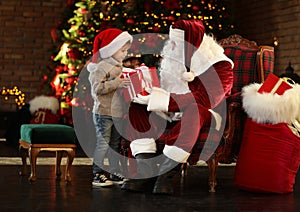 Santa Claus and little boy with gift near Christmas tree