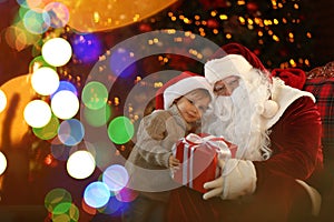 Santa Claus and little boy with gift near Christmas tree