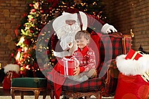 Santa Claus and little boy with gift near Christmas tree