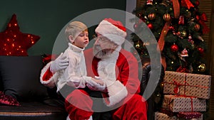 Santa Claus with little boy sitting on his lap and talking about his dreams. Grandson and grandfather sitting in