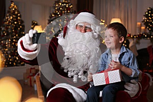 Santa Claus and little boy taking selfie in room decorated for Christmas