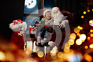 Santa Claus and little boy with toy train near window. Christmas holiday