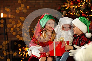 Santa Claus and little children with present near Christmas tree