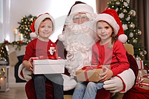 Santa Claus and little children with presents in room decorated for Christmas