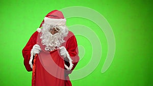 Santa Claus looks in a bag with gifts on green background