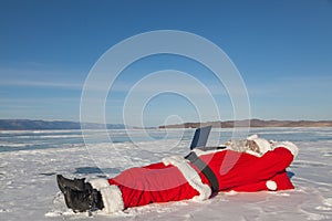 Santa Claus lying on the snow, looking at laptop news