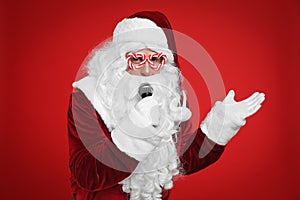 Santa Claus with microphone singing on red background. Christmas music