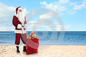 Santa Claus near sack of gifts on sandy beach. Space for text