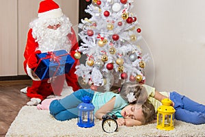 Santa Claus in New Years Eve gifts lays out and looked at the fallen asleep in front of Christmas tree two children