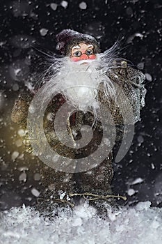 Santa Claus Outdoors Beside Christmas Tree in Snowfall Carrying Gifts to Children