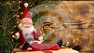 santa claus plush toy with a big white beard sits on a Christmas present with a red bow near the