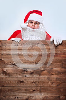 Santa Claus pointing in blank advertisement wooden banner with copy space