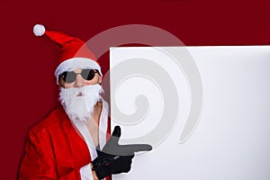 Santa Claus pointing at blank promotional banner with copy space on red background.