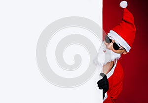 Santa Claus pointing at blank promotional banner with copy space on red background.