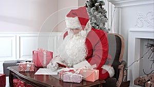 Santa Claus preparing presents for children and checking the gift list