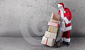 Santa Claus with presents stacked on a delivery trolley with a plain background and copy space