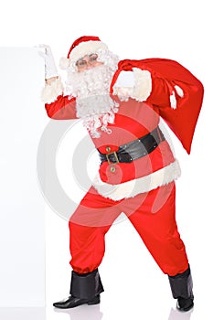 Santa Claus pushes blank white wall, advertisement banner with copy space while carrying on big bag. Isolated on white