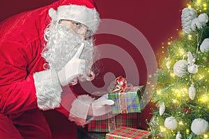 Santa Claus putting gift box or present under Christmas tree