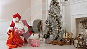Santa Claus putting presents back into his bag by Christmas tree photo
