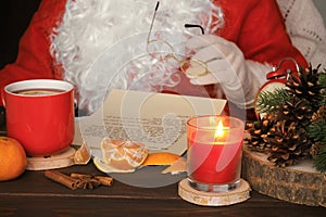 Santa Claus reading letter, drinking tea and eating tangerines.