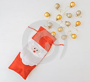 Santa Claus red bag with yellow and gold Christmas toys on white wooden background