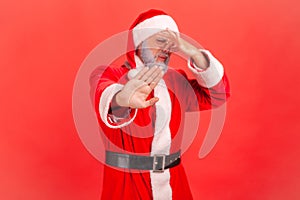 Santa claus in red costume pinching nose with fingers to avoid bad smell and showing stop gesture